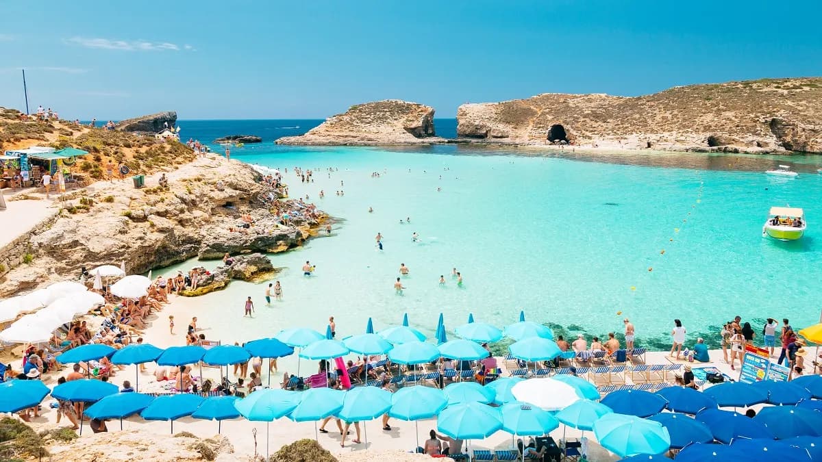 La Blue Lagoon en verano, con bañistas en el agua turquesa y sombrillas en la orilla de roca