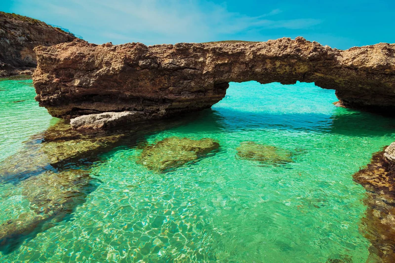 Arco de roca natural sobre el agua verde turquesa y transparente de la Blue Lagoon, con el fondo de roca a la vista