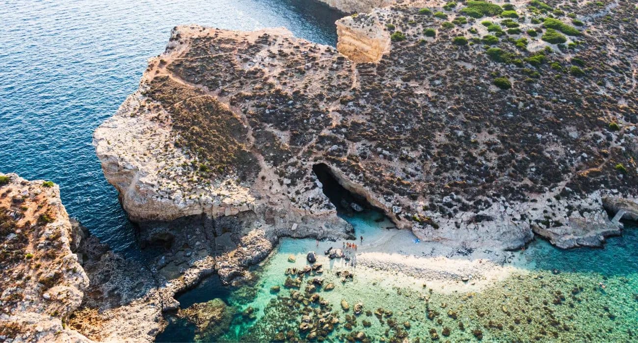 La pequeña cala de arena de Cominotto vista desde el aire, con una cueva en la roca y el agua turquesa