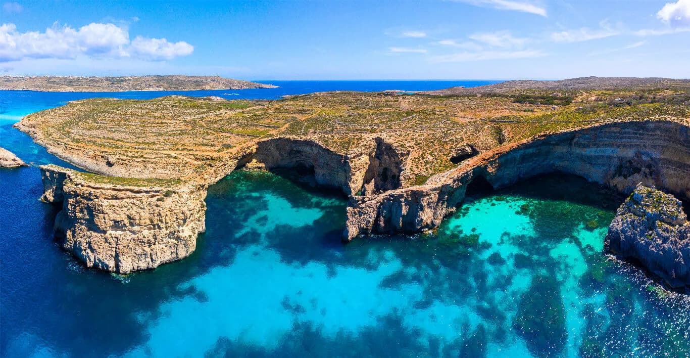 La Crystal Lagoon de Comino desde el aire: agua turquesa entre acantilados con cuevas