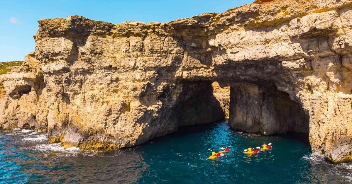 Kayaks entrando en las Santa Maria Caves, cuevas abiertas en el acantilado de Comino sobre el agua azul oscuro