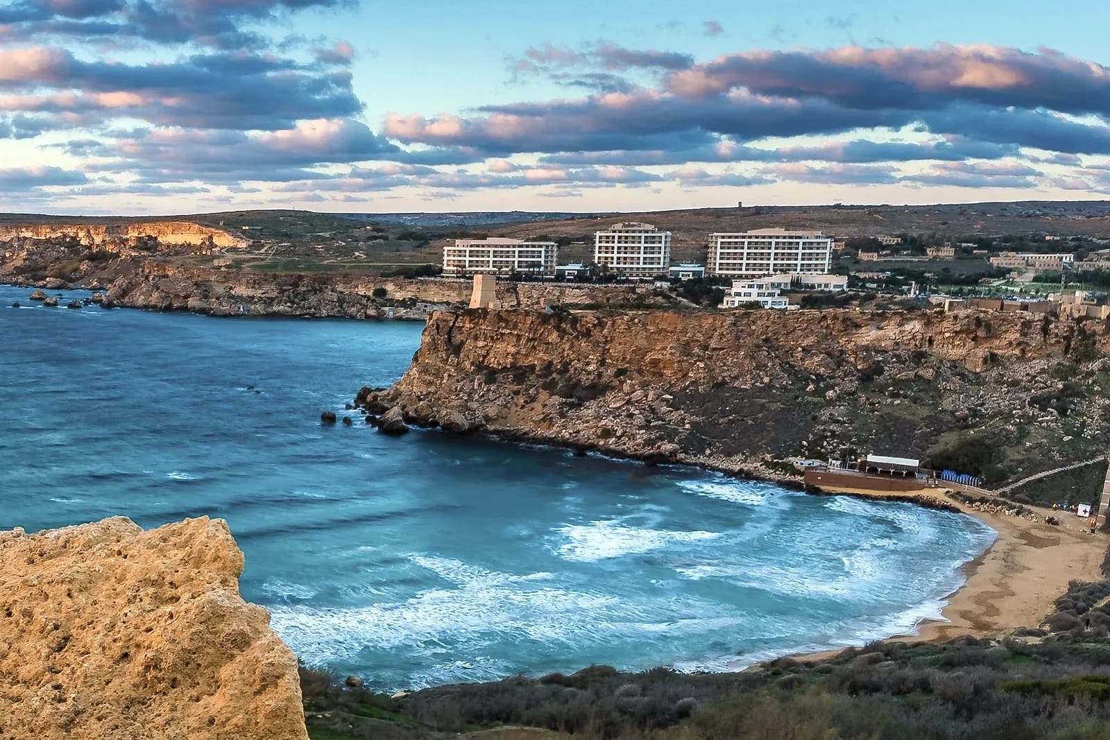 Għajn Tuffieħa (Riviera Bay) desde el camino de Il-Qarraba: la playa de arena con el beach club, el acantilado con la torre y, detrás, los hoteles de Golden Bay