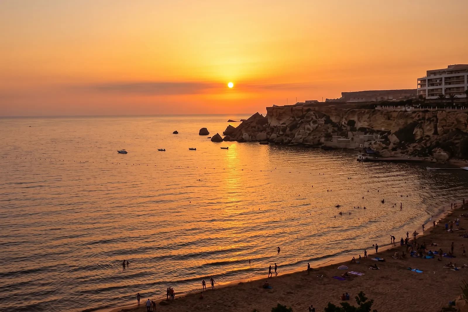 Puesta de sol sobre el mar en Golden Bay, con bañistas en la orilla y el acantilado a la derecha
