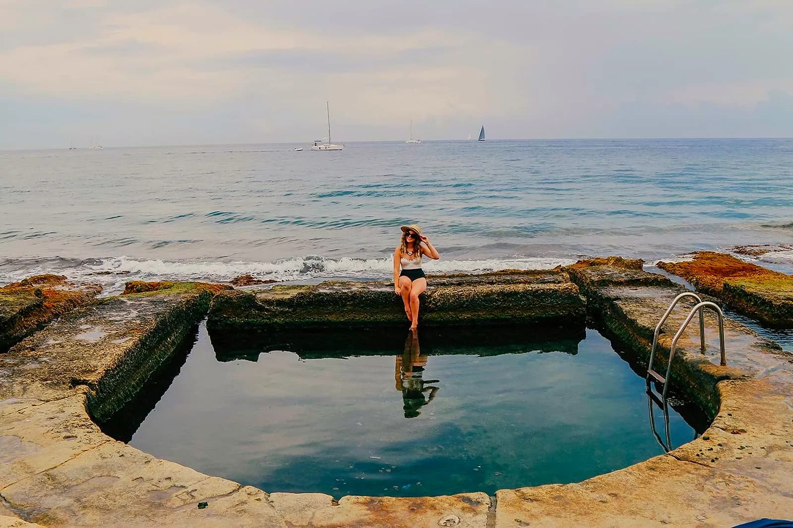 Una bañista sentada en el borde de una de las piscinas victorianas excavadas en la roca de Sliema, con el mar detrás