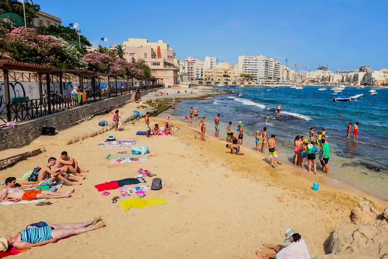 La pequeña playa de arena de Exiles, en Sliema, con bañistas y los edificios de la costa al fondo