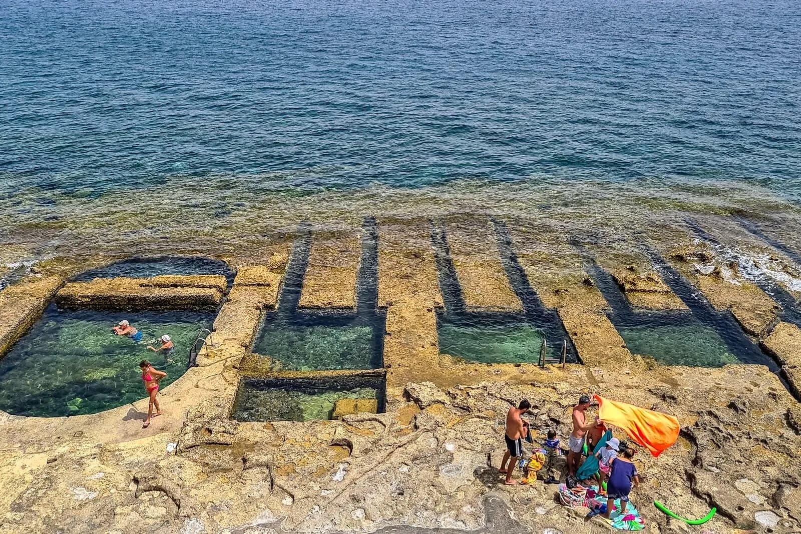 Hilera de baños victorianos excavados en la roca de Sliema, con el mar al fondo